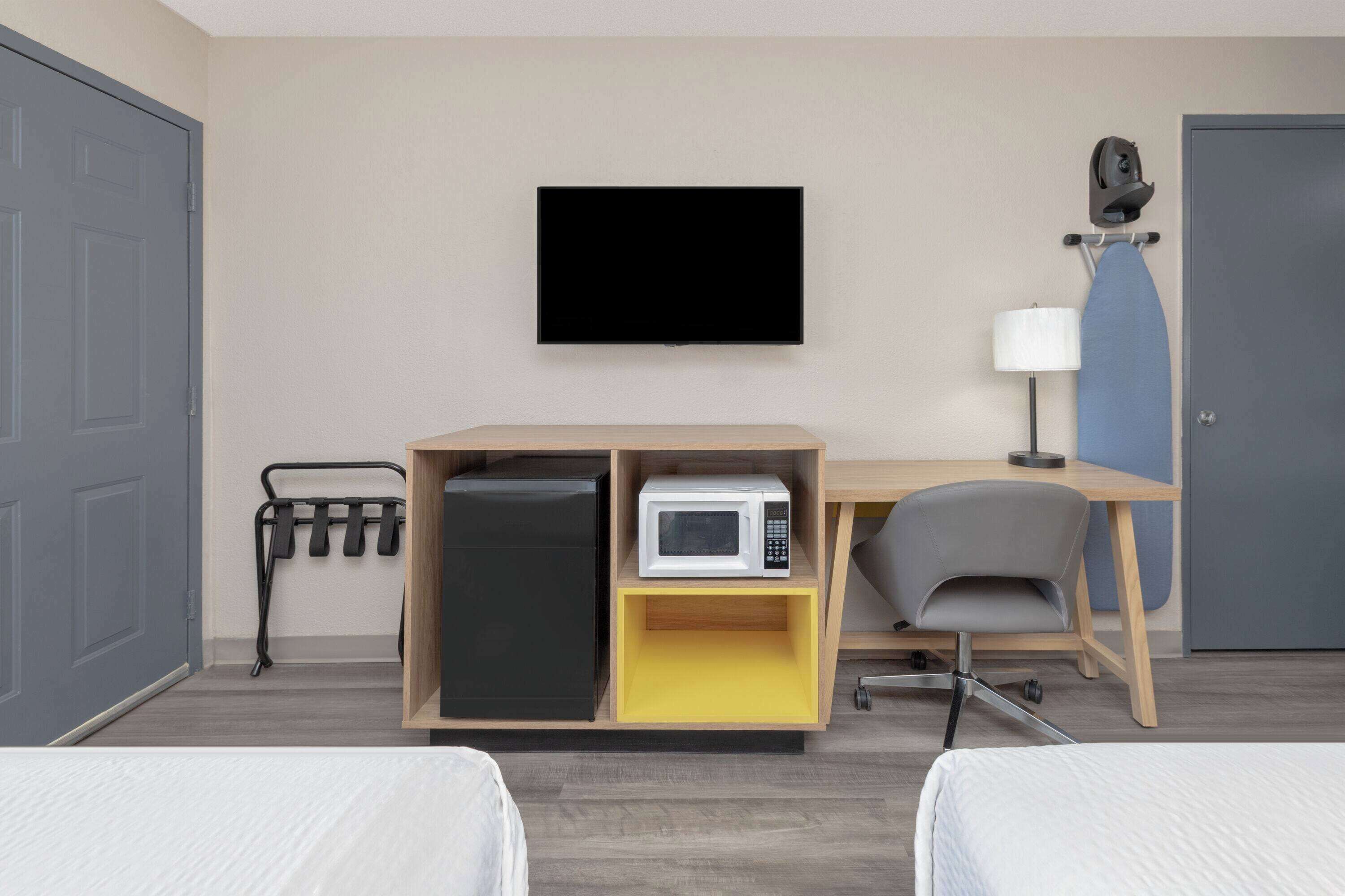 A hotel room with a bed, a desk with a computer, a microwave, and a TV on the wall.