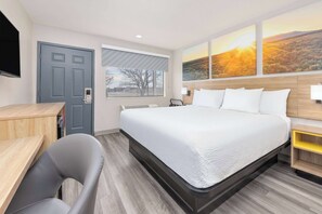 Une chambre d’hôtel moderne, dotée d’un grand lit, d’un bureau, d’une chaise et d’une fenêtre donnant sur un paysage.