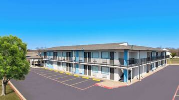 A motel with a two-story structure, a parking lot, and a tree.