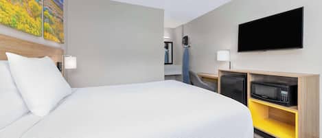 Habitación de hotel con una cama grande, un televisor de pantalla plana, un microondas y una pequeña zona de estar con una silla y una mesa.