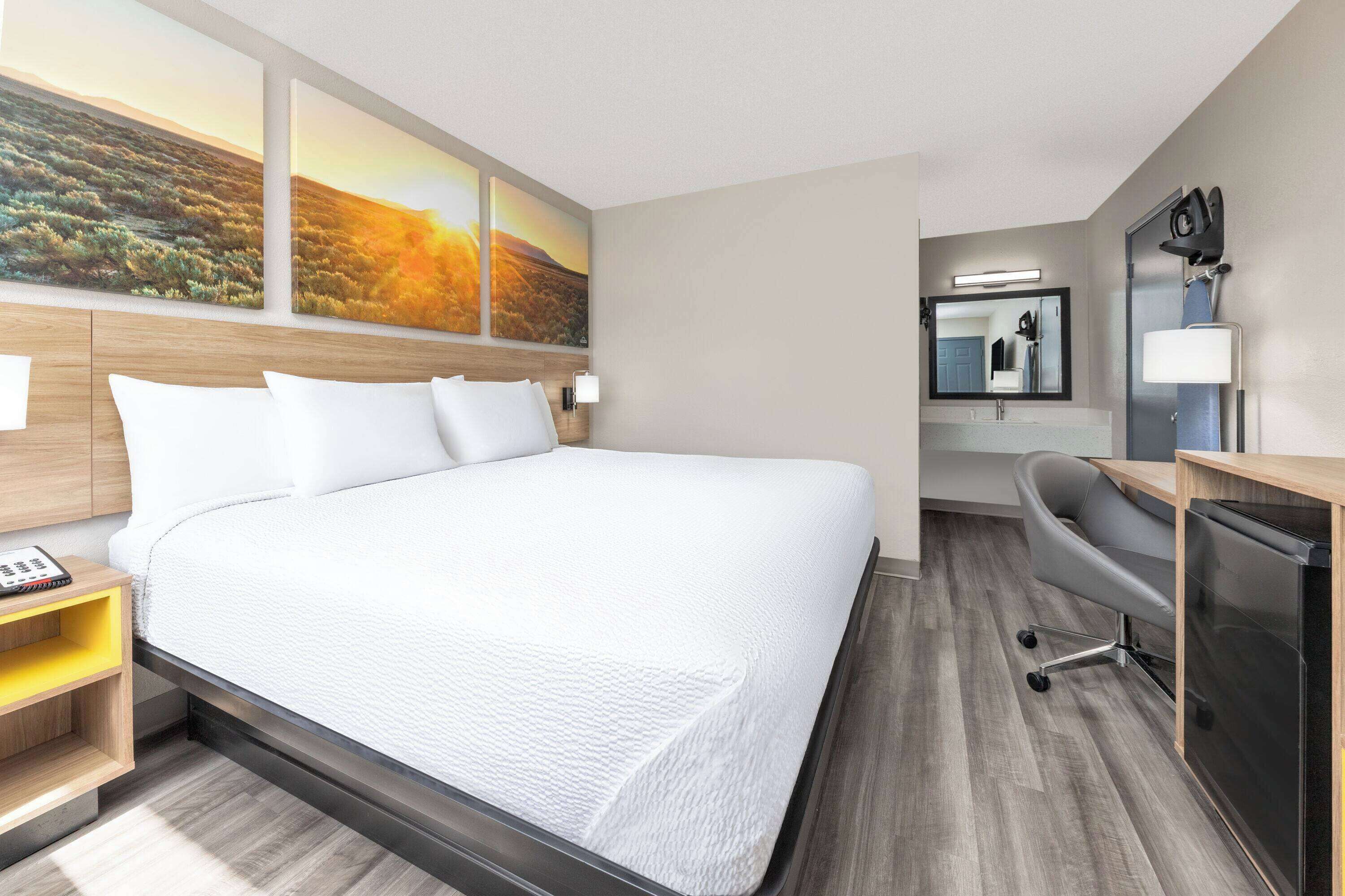 Ein Hotelzimmer mit einem großen Bett, einem Schreibtisch mit Stuhl, einem Spiegel und Bildern an der Wand.