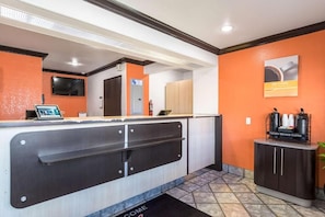 A reception area with a counter, a digital screen, a coffee station, and a door marked with an elevator symbol. - Motel 6 Riverside, CA - UCR East (Riverside)
