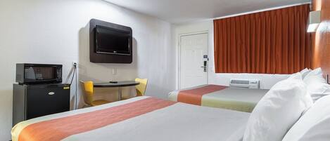A hotel room with two beds, a desk with a microwave, a TV, and a window with curtains.