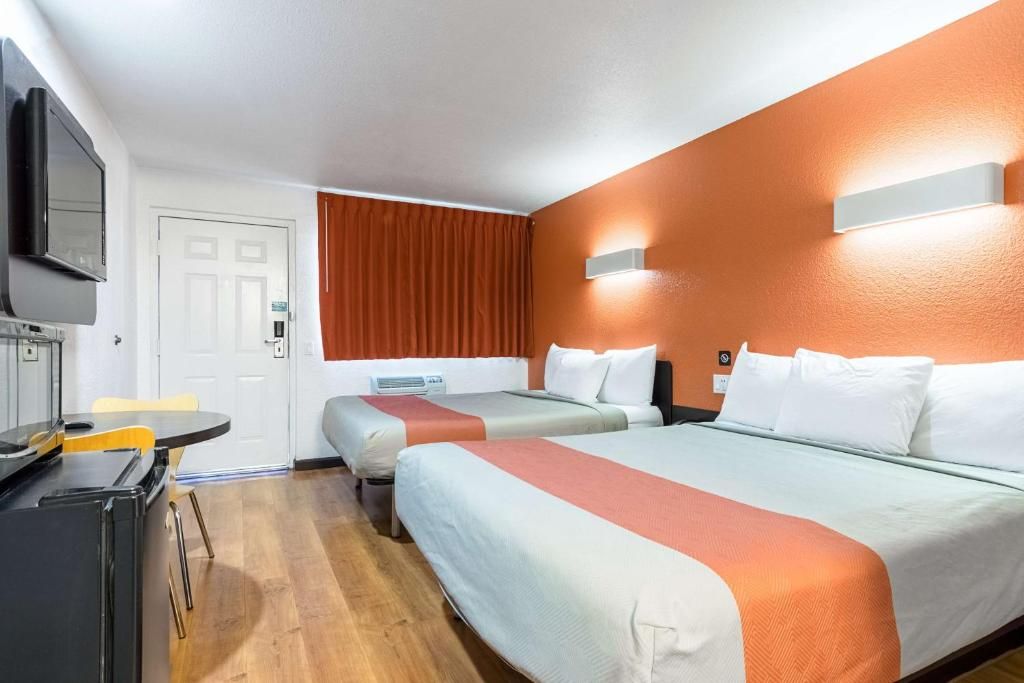 A hotel room with two beds, a desk, a television, and a window with curtains.