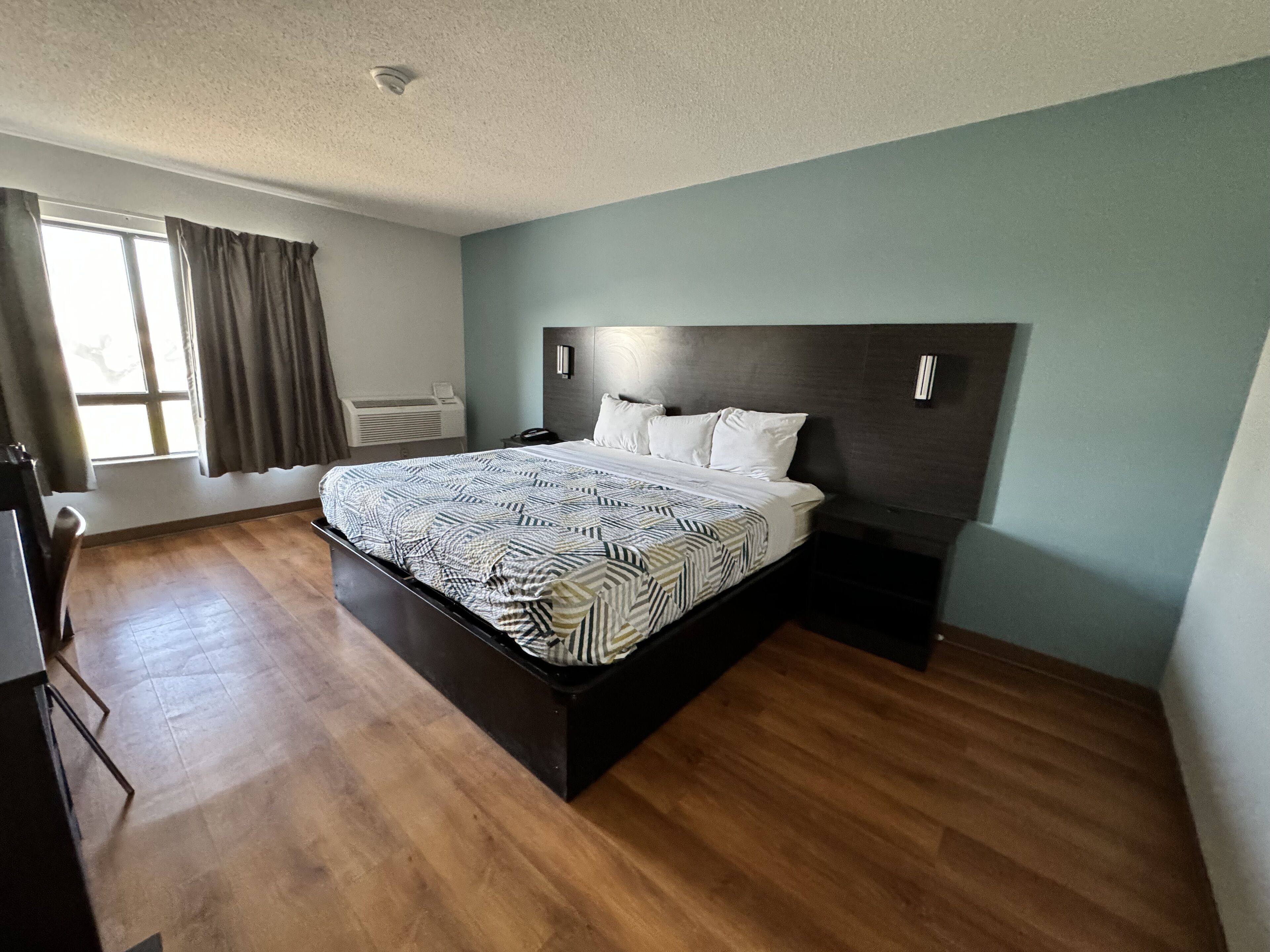 Een moderne slaapkamer met een groot bed, houten vloer, een raam met gordijnen en een ingebouwde airconditioning.
