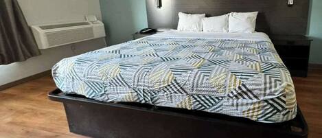 Una habitación de hotel con cama, mesita de noche, equipo de aire acondicionado y lámpara de pared.