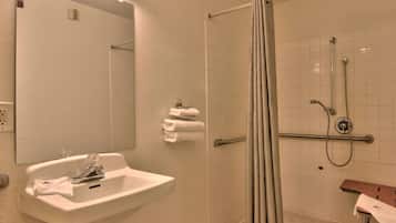 Une salle de bain équipée d’un lavabo, d’un miroir, d’un porte-serviettes, d’une douche et d’un banc en bois.