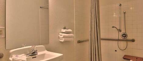 Une salle de bain équipée d’un lavabo, d’un miroir, d’un porte-serviettes, d’une douche et d’un banc en bois.