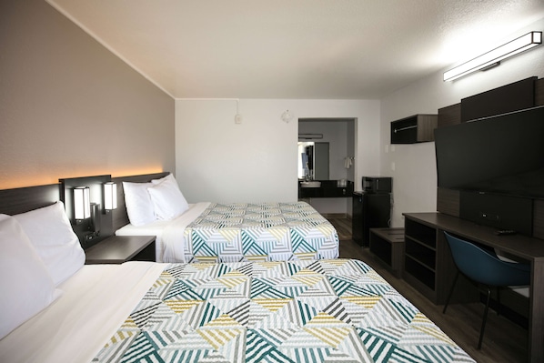 A hotel room with two beds, a desk, a chair, a TV, and a mirror.