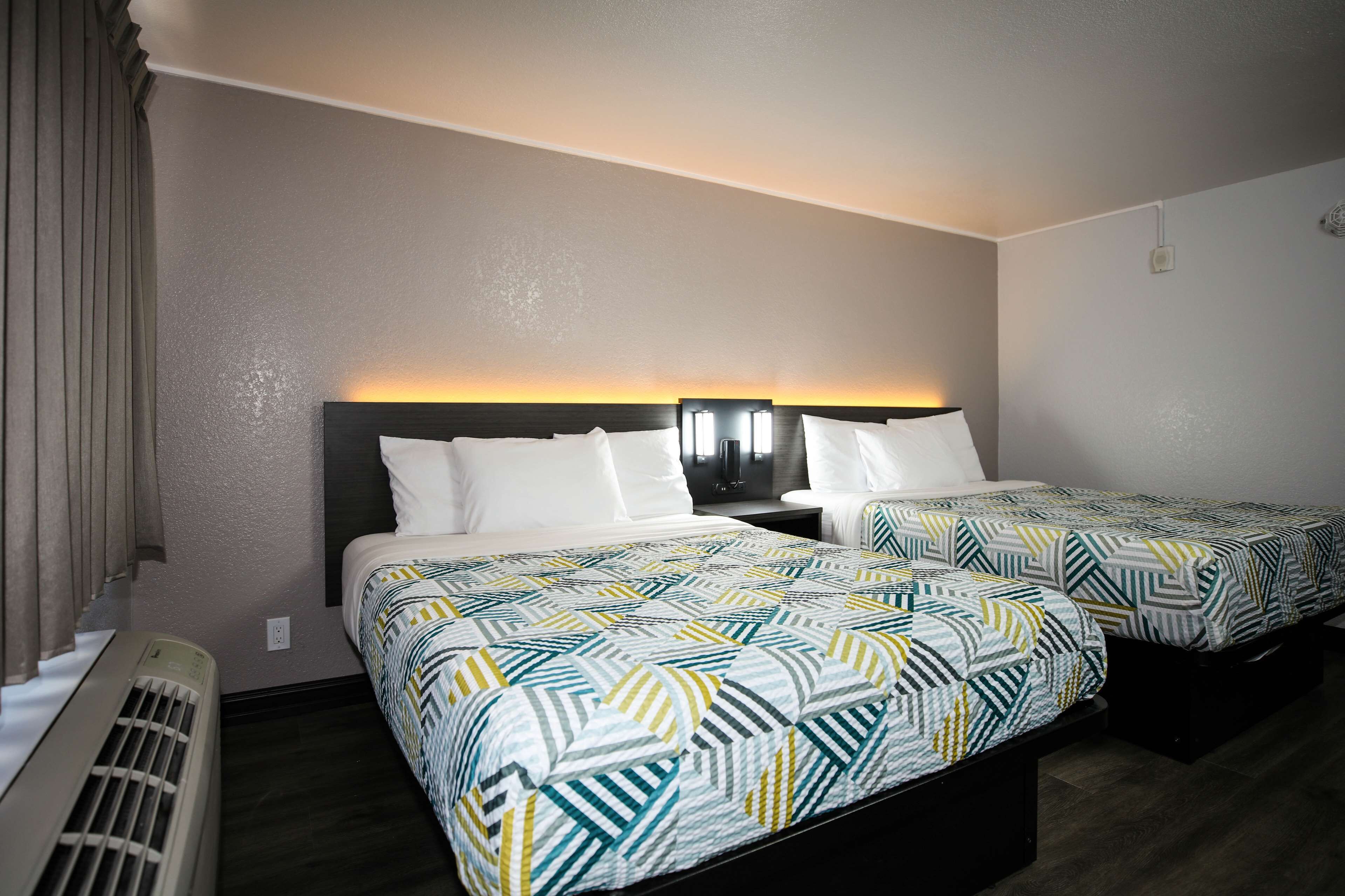 A hotel room with two beds, a nightstand, a heater, and a window with curtains.
