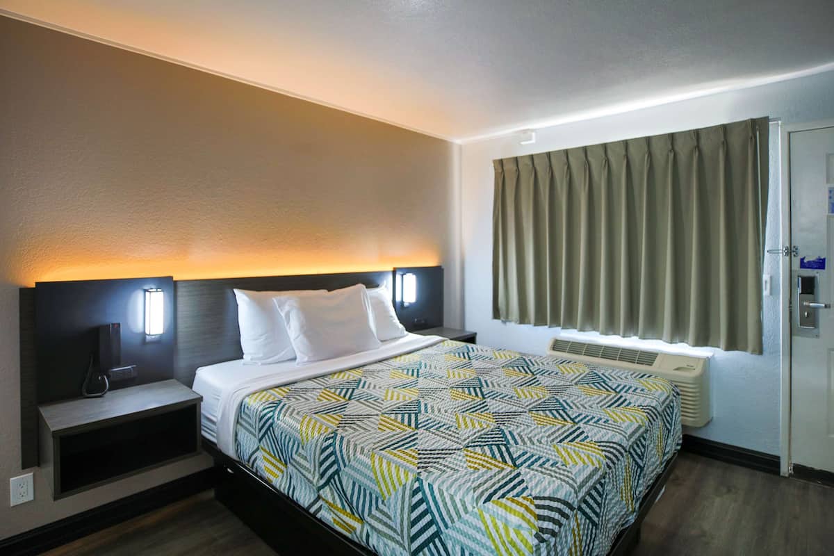Ein Hotelzimmer mit Bett, Nachttisch, Wandfernseher und einem Fenster mit Vorhängen.