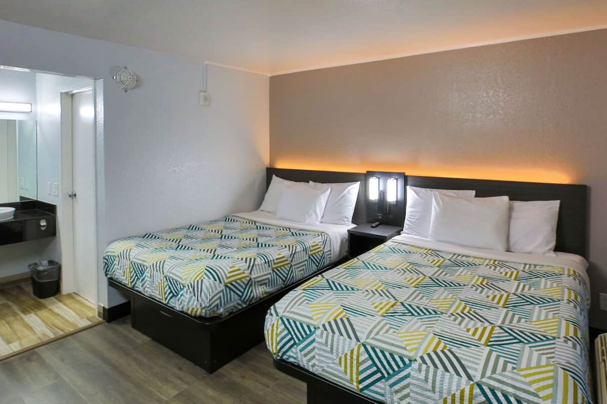 Ein Hotelzimmer mit zwei Betten, einem kleinen Badezimmer und einer Tür zu einem anderen Raum.