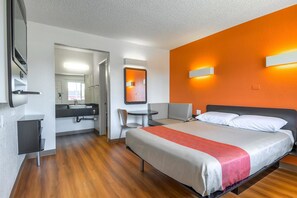 A hotel room with a bed, a desk, a chair, a bathroom with a mirror, and a window. - Motel 6 Long Beach, CA - Los Angeles (Long Beach)