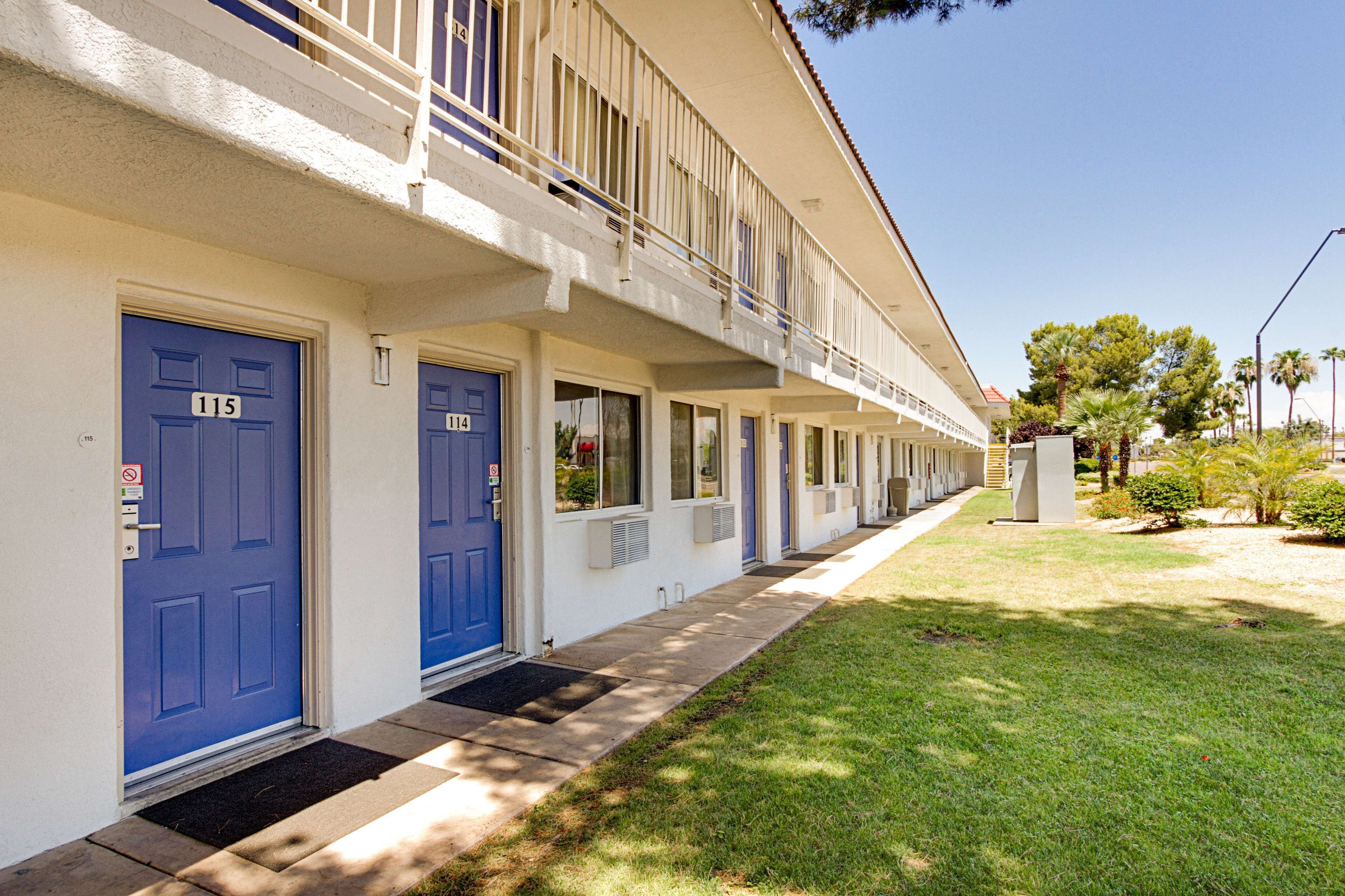 A row of blue doors with numbers 115 and 114, indicating a hotel or apartment building with a uniform facade and a small front yard.