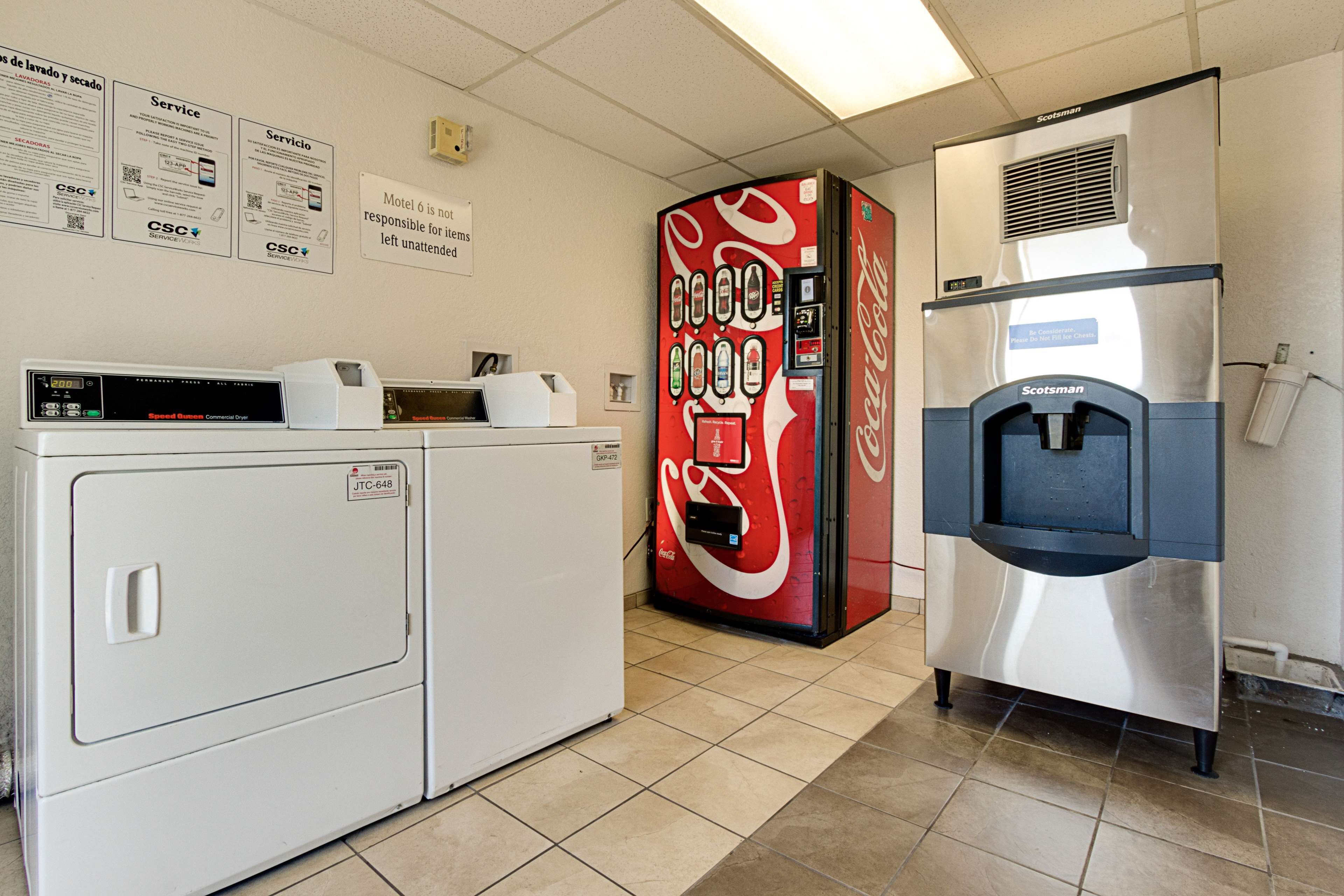 Habitación de hotel con lavadora, máquina expendedora de Coca-Cola y refrigerador de acero inoxidable.