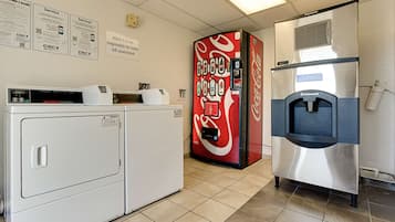 Habitación de hotel con lavadora, máquina expendedora de Coca-Cola y refrigerador de acero inoxidable.