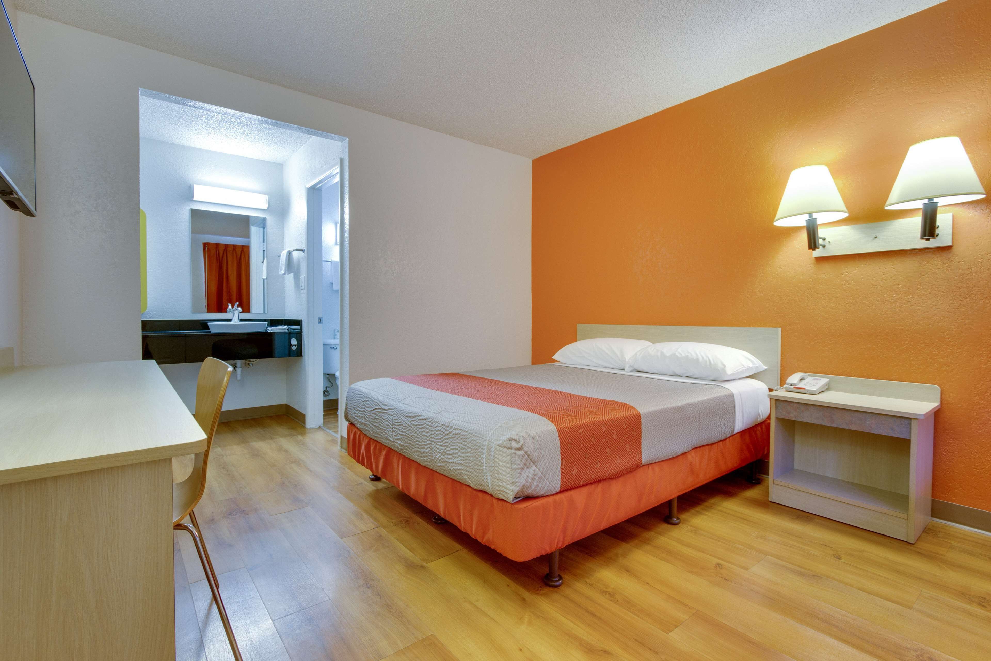 A hotel room with a bed, bedside table, and a desk with a chair.