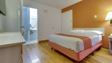 Une chambre d’hôtel avec un lit, un bureau, une salle de bain visible à travers une porte ouverte et une lampe fixée au mur.