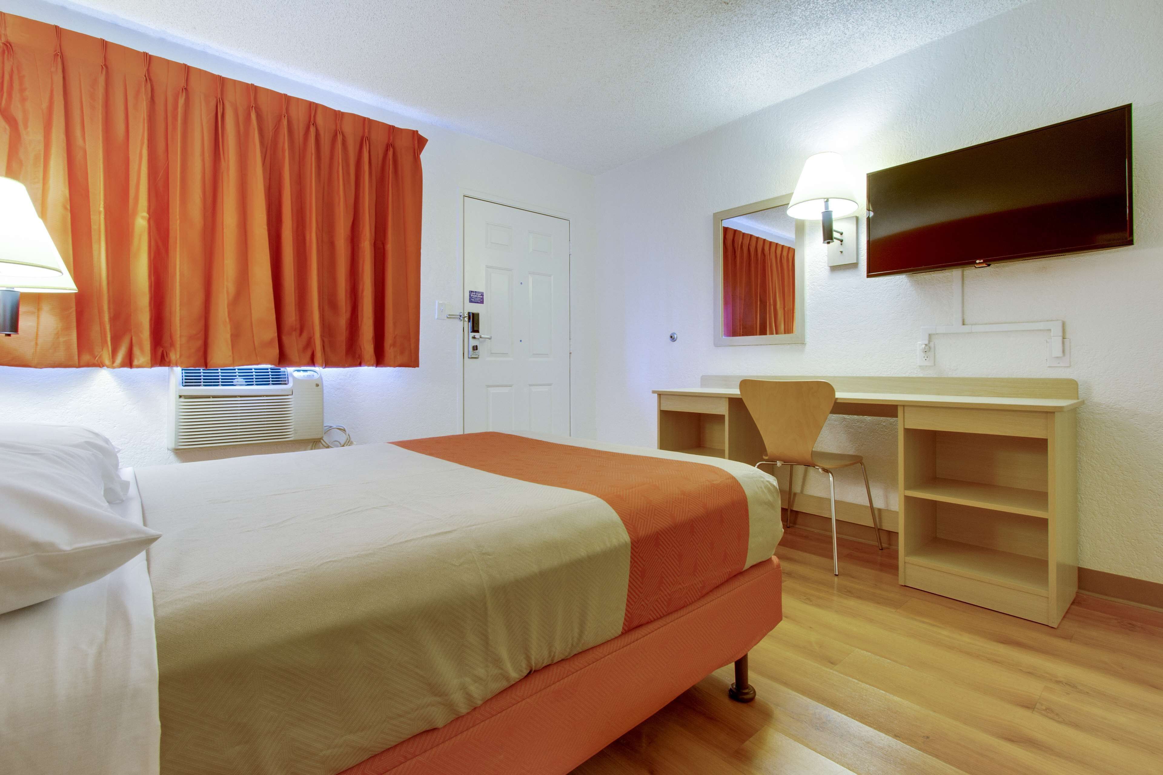 Una camera d'albergo con un letto, una scrivania, una sedia, una televisione e un condizionatore d'aria.