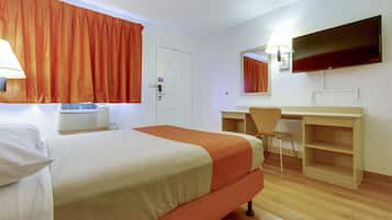Een hotelkamer met een bed, bureau, stoel, televisie en een airconditioning.
