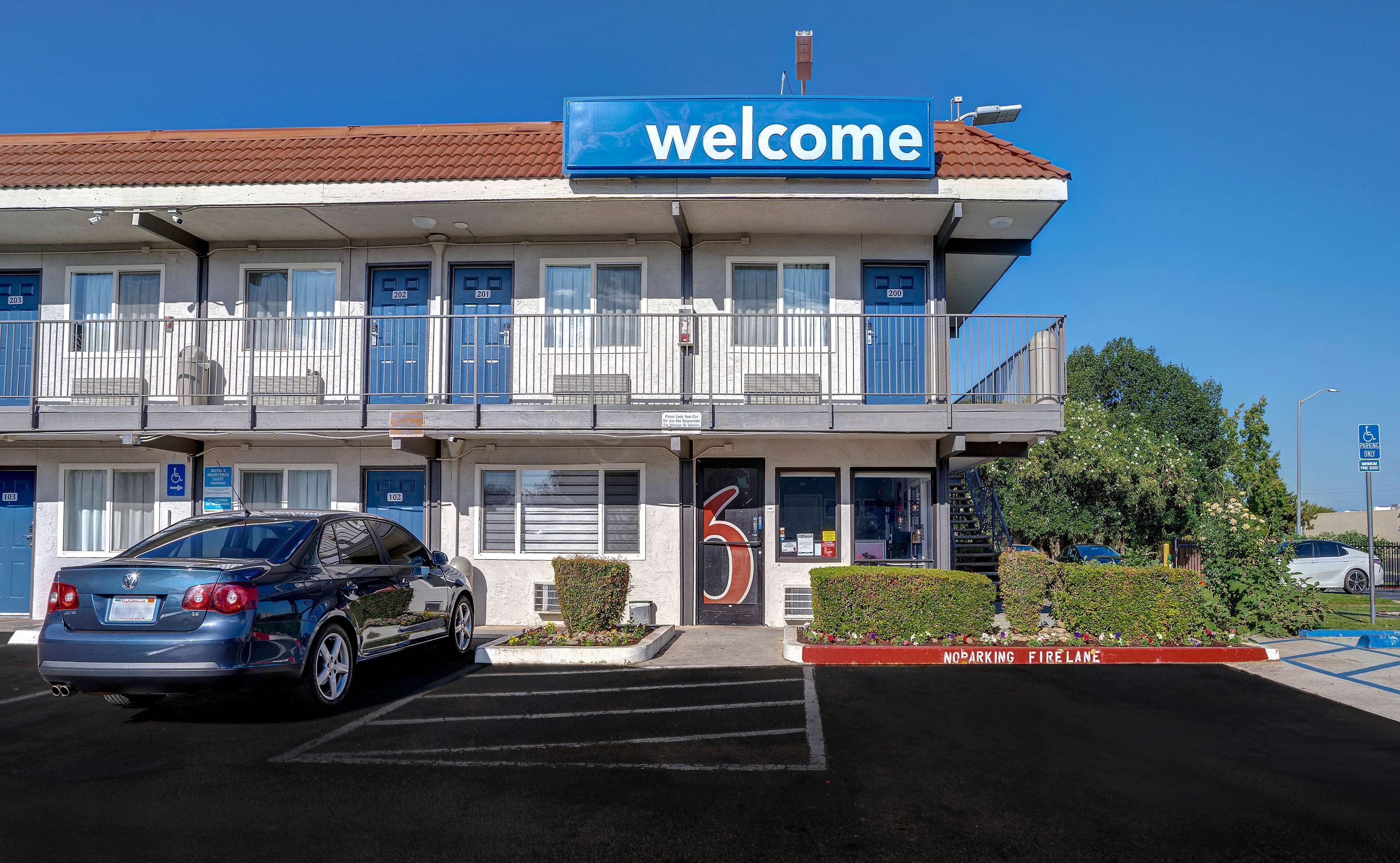 A hotel with a 'Welcome' sign, numbered rooms, a fire lane, and a disabled parking sign.