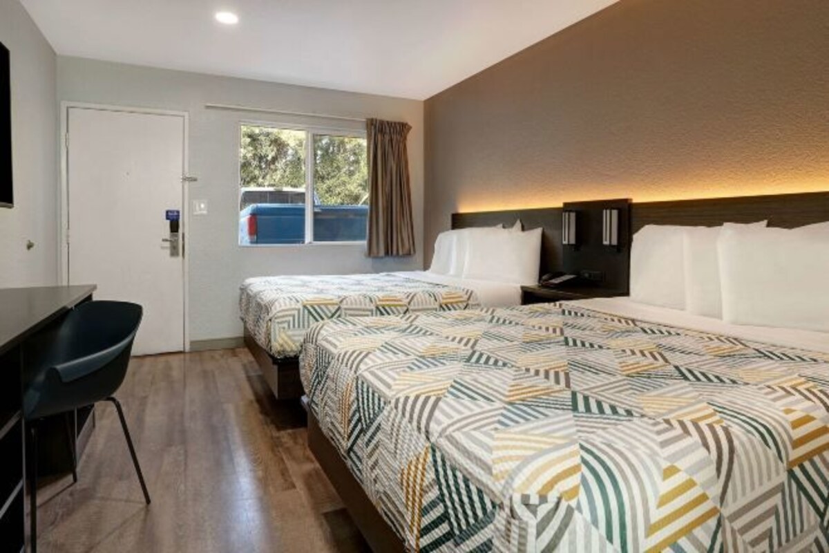 A hotel room with two beds, a desk, and a chair.