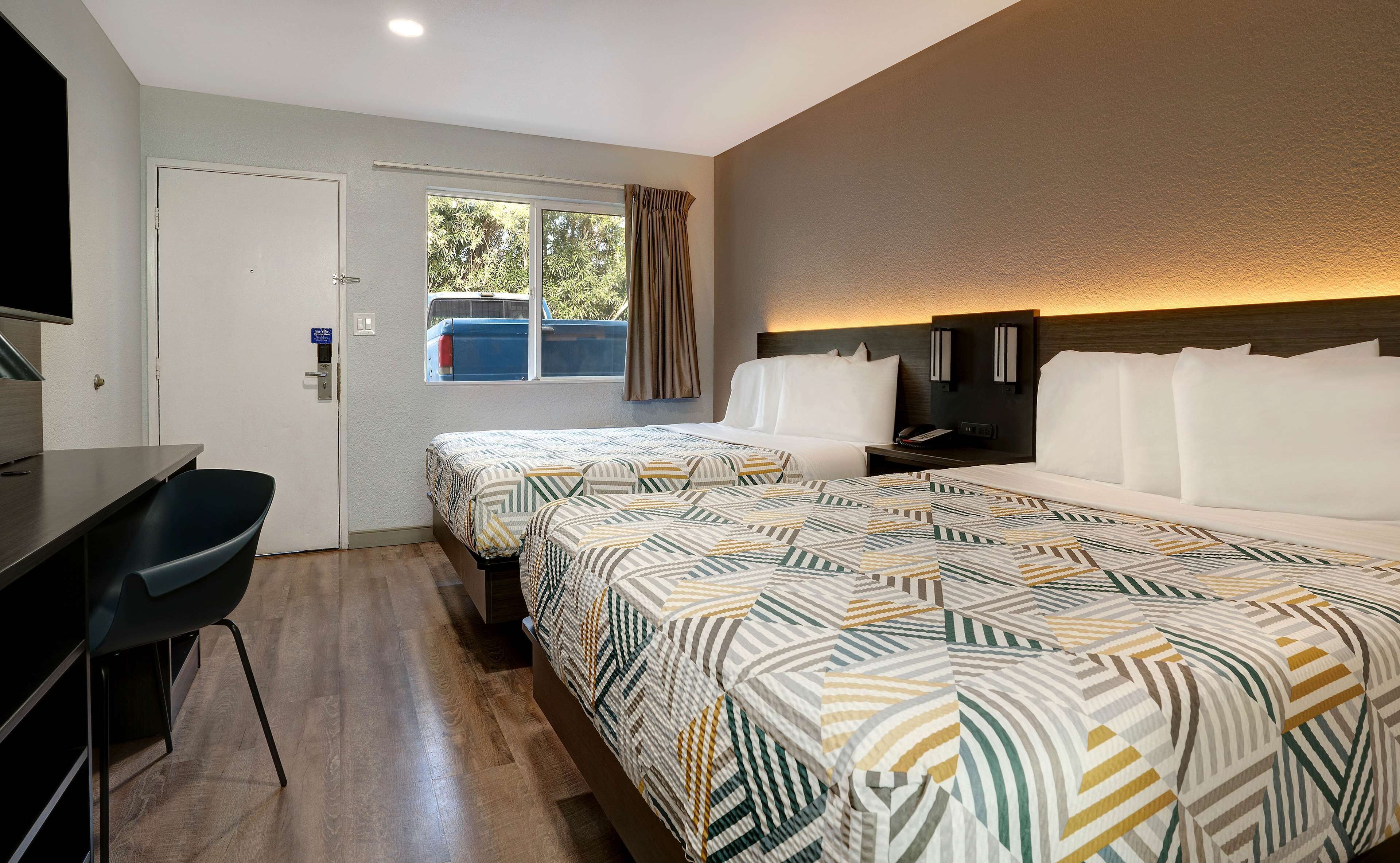 Habitació d'hotel amb dos llits, una taula de treball, una cadira, una televisió i una finestra amb cortines.