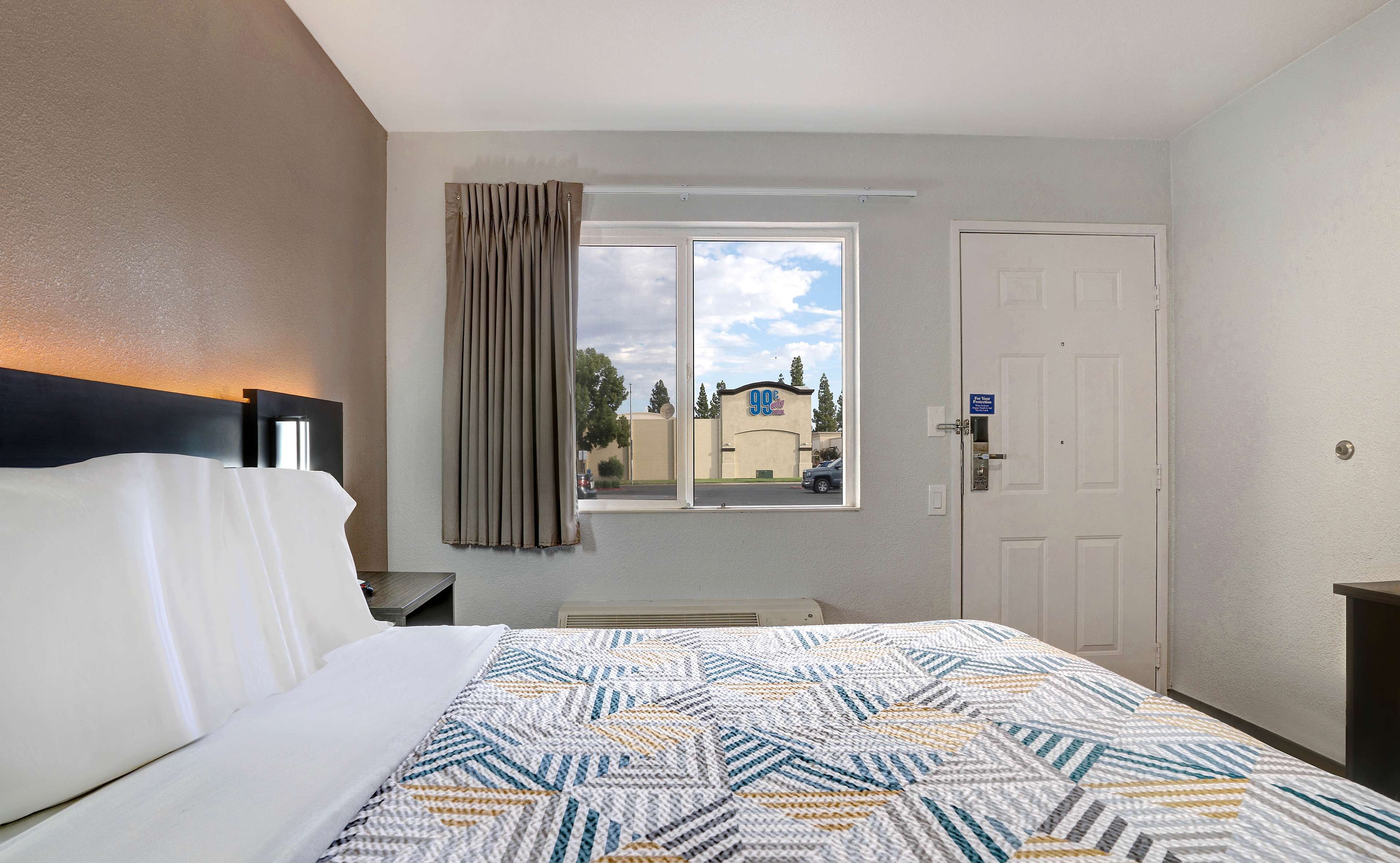 Una habitación de hotel con cama, ventana con cortinas, puerta y vistas al exterior.