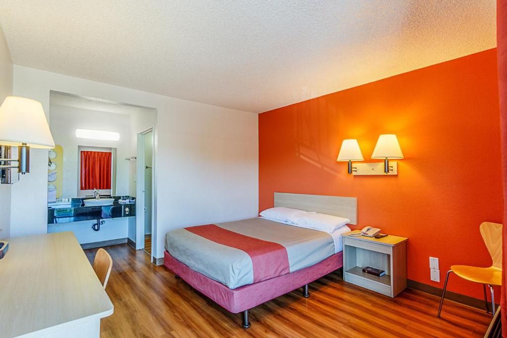 A hotel room with a bed, bedside table, lamp, and a small desk with a chair.