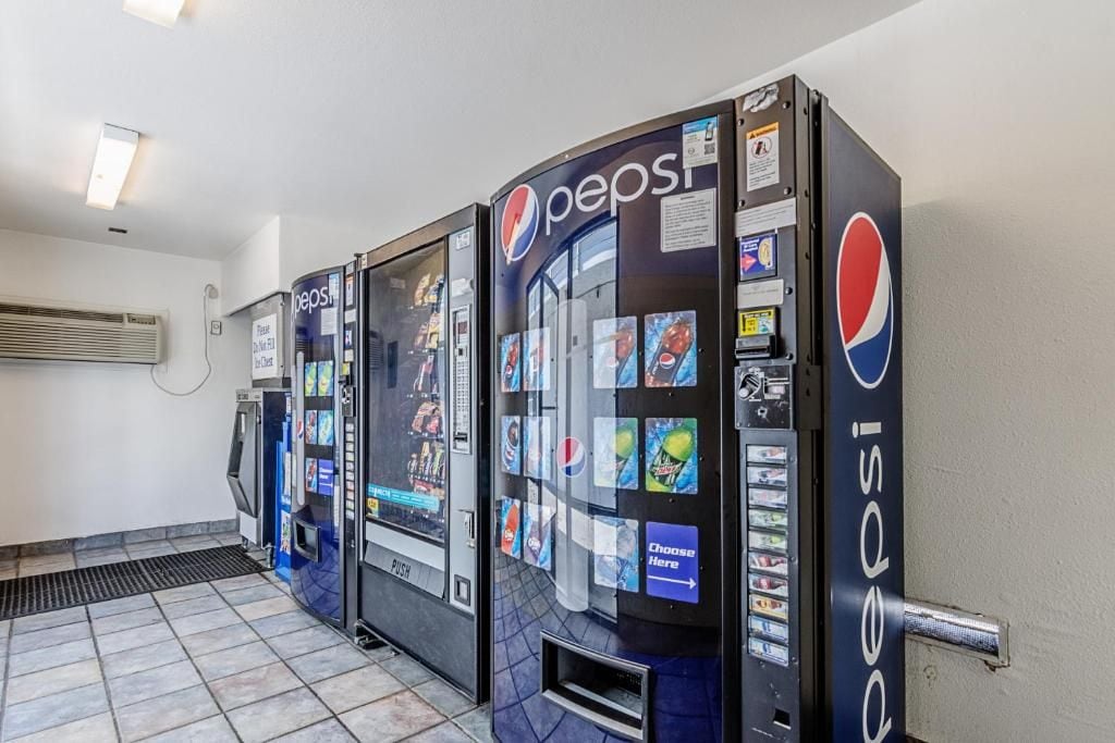 Three Pepsi vending machines in a room with tiled flooring and a wall-mounted air conditioning unit.