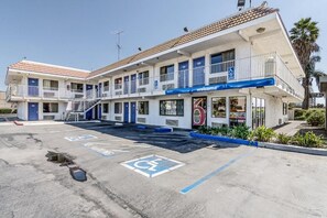 Un motel con una estructura de dos pisos, un toldo azul y un espacio de estacionamiento para discapacitados.