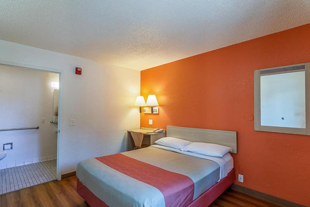 A hotel room with a bed, bedside lamps, a nightstand, and a door leading to a bathroom.