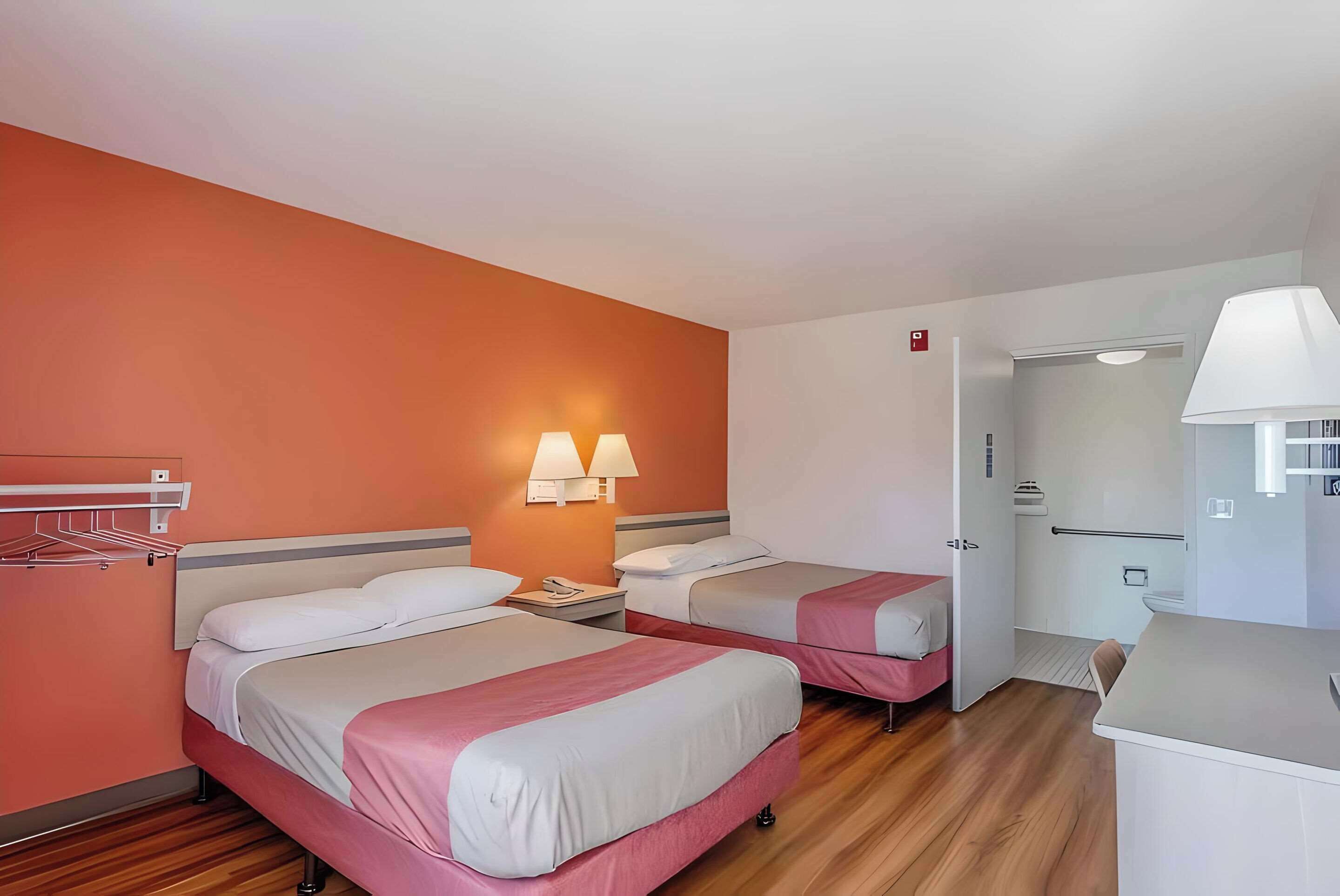 A hotel room with two beds, a desk, a chair, a lamp, a wardrobe, and a bathroom.