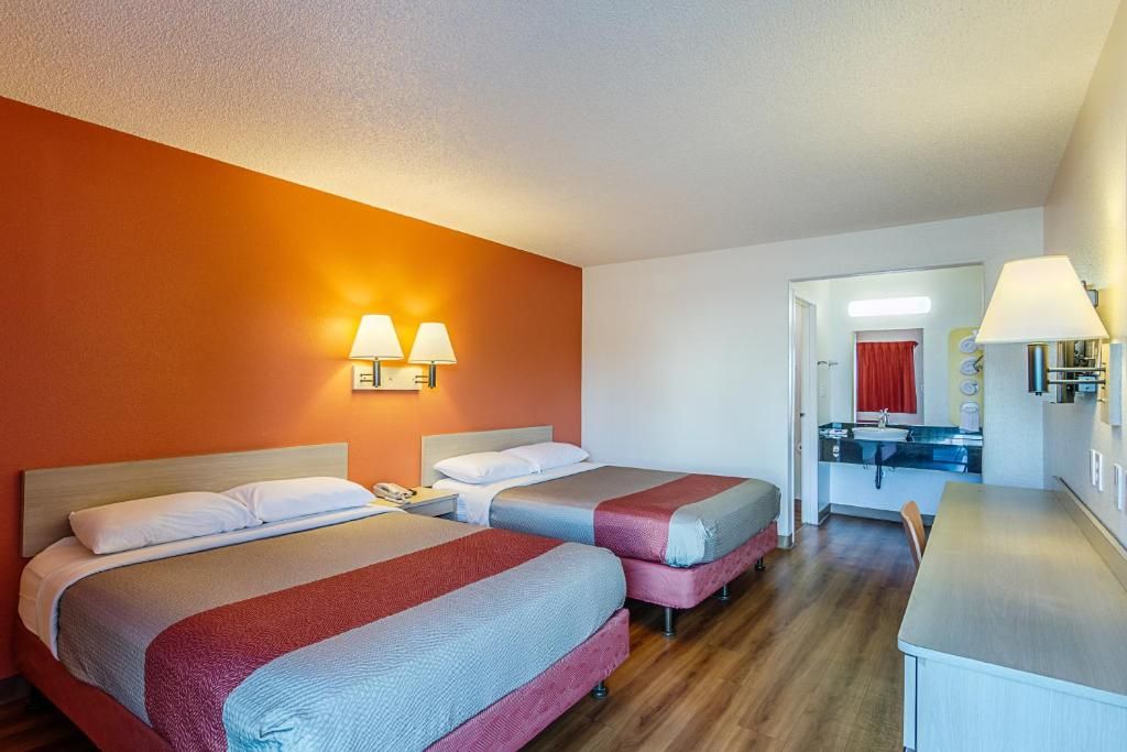 A hotel room with two beds, a desk, and a bathroom visible through an open door.