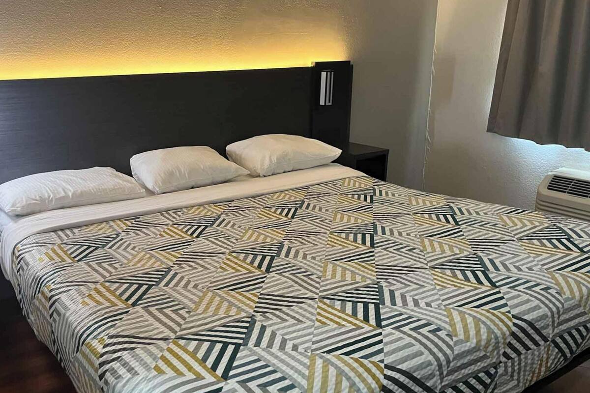 A hotel room with a bed, nightstands, a wall-mounted lamp, and a window with curtains.