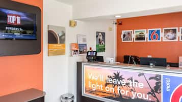 A hotel reception area with a TV displaying 'TOP 10 SUNDAYS 9p', a digital kiosk, and a 'motel' sign.