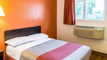 A hotel room with a bed, a window with curtains, and an air conditioning unit.