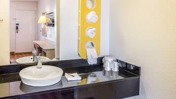 A bathroom with a black countertop, a white sink, a mirror, and a towel rack with three towels.