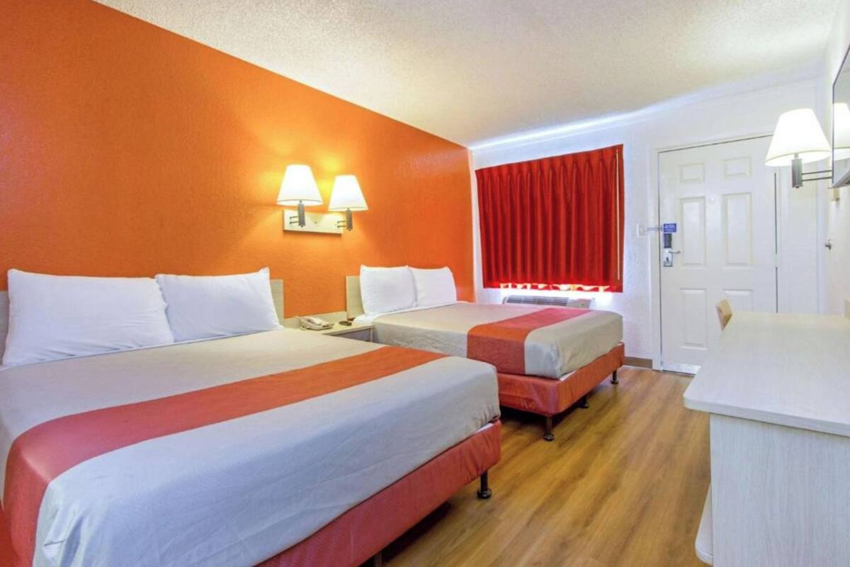 Habitación de hotel con dos camas, un escritorio, una silla, una cortina roja y una puerta blanca.
