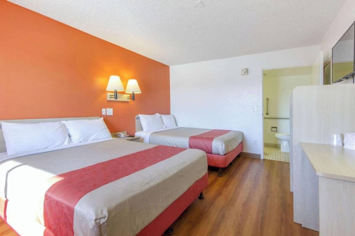 Habitación de hotel con dos camas, baño y una pequeña cocina.