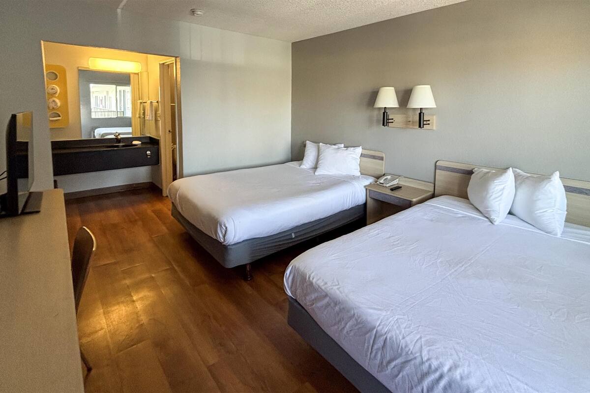 Une chambre d’hôtel avec deux lits, un bureau, un miroir et une salle de bain équipée d’un lavabo et d’un porte-serviettes.