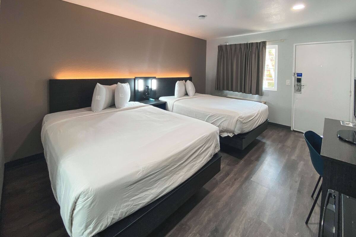 A hotel room with two beds, a desk, and a chair.