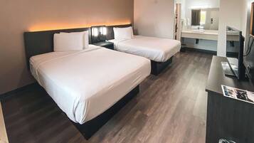 A hotel room with two beds, a desk, a mirror, and a bathroom visible through an open door.