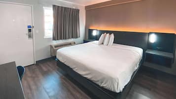 Habitación de hotel con una cama grande, un escritorio, una ventana con cortinas, un aire acondicionado y dos lámparas de noche.