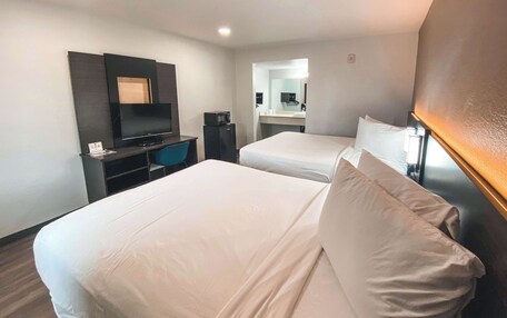 A hotel room with two beds, a desk with a computer, a TV, and a bathroom visible through an open door.