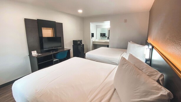 Une chambre d’hôtel avec deux lits, un bureau avec un ordinateur, une télévision et une salle de bain visible à travers une porte ouverte.