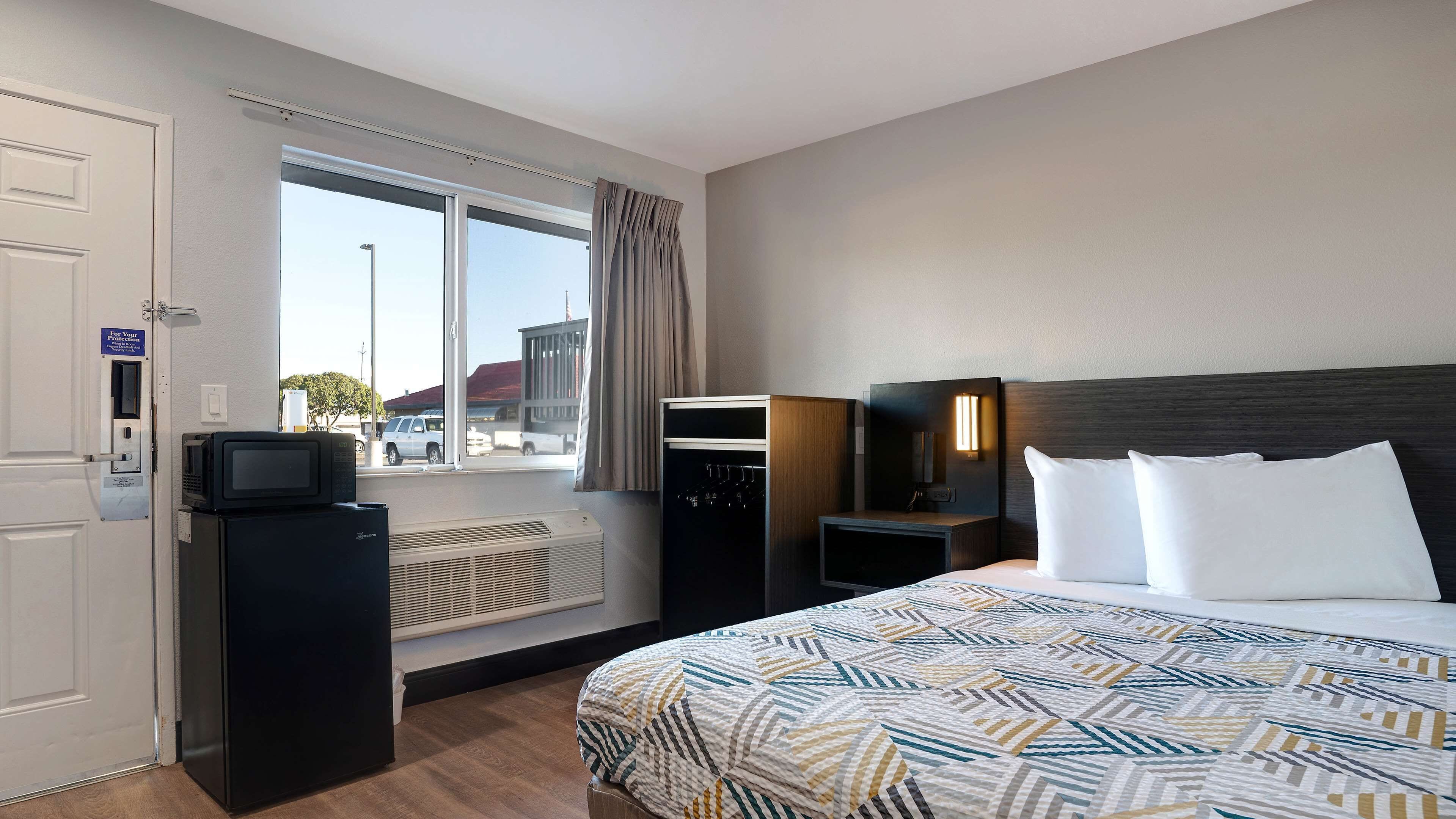 Una habitación de hotel con cama, escritorio, televisor y ventana con cortinas.