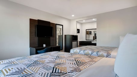 A hotel room with two beds, a desk, a television, a mirror, and a small refrigerator.