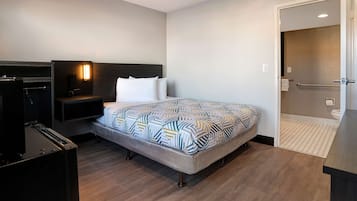 A hotel room with a bed, a TV, a nightstand, a wall-mounted light, and a bathroom visible through an open door.