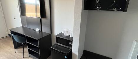 A compact room with a built-in desk, a small refrigerator, a microwave, and a wall-mounted TV.